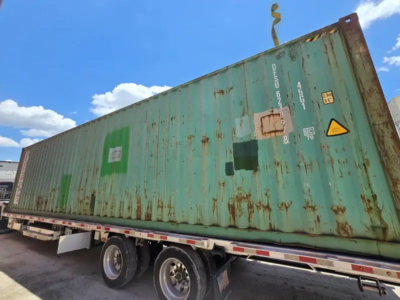 A side view of a cargo-worthy 40ft high cube container on a delivery truck, preparing for unloading.