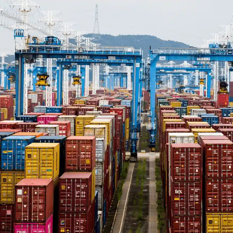 Vast container terminal with hundreds of stacked multi-colored containers and huge blue overhead gantry cranes.