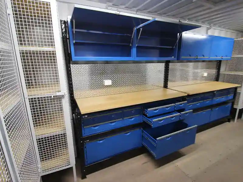 Professional container workshop interior with blue drawers, wood workbench, diamond-plate backsplash, and secure mesh locker.