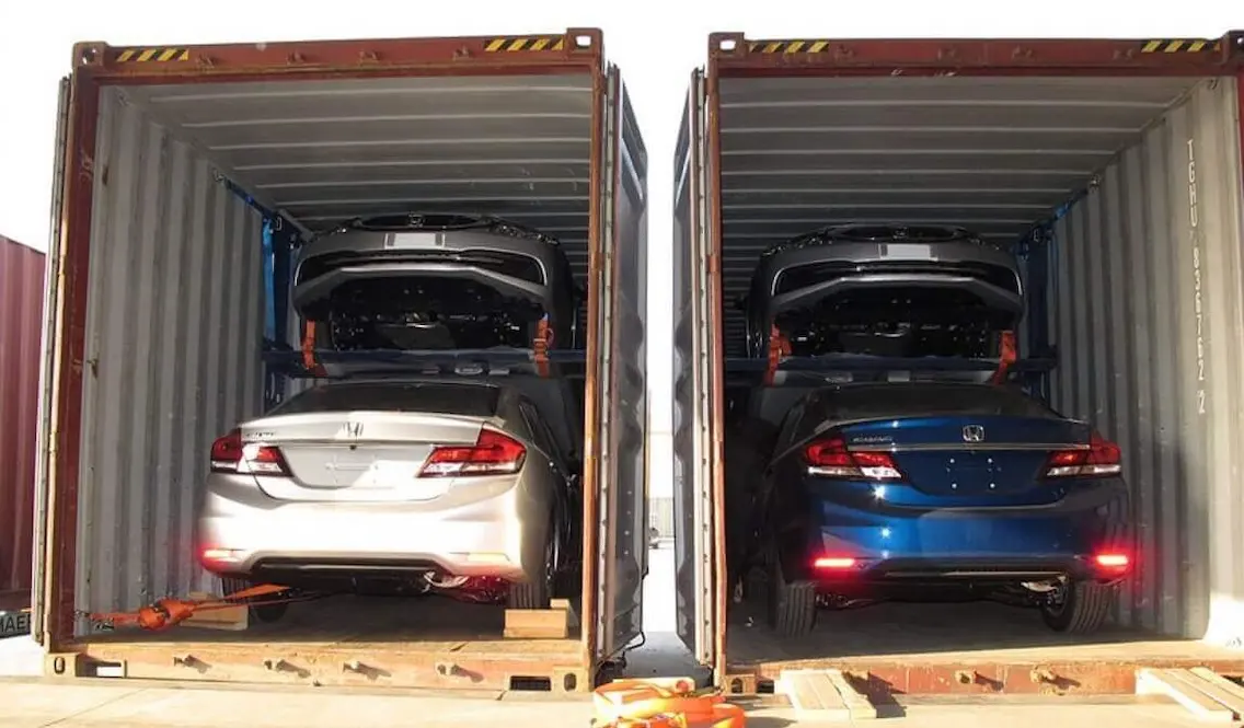 Two shipping containers side-by-side, each loaded with two cars using specialized internal racking systems for secure vehicle export.