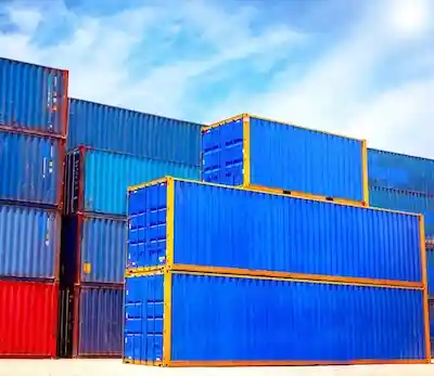 Bright blue shipping containers with yellow trim stacked high in a depot, showcasing new and used inventory volume.