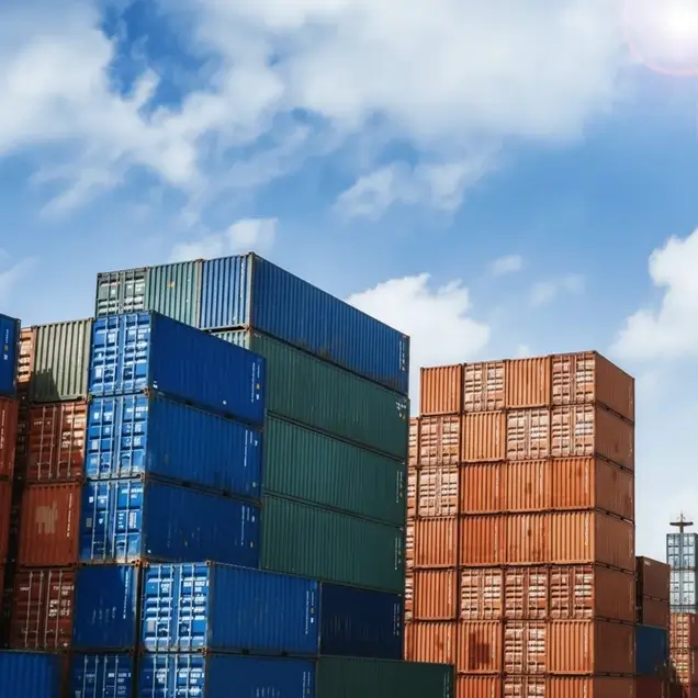 Massive stacks of colorful 20ft and 40ft intermodal shipping containers at a busy cargo port under a blue sky, symbolizing global inventory and supply.