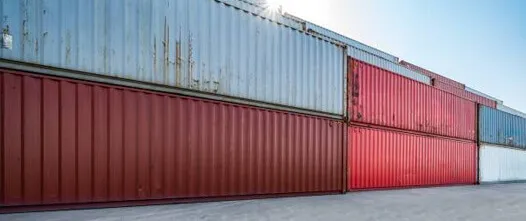 Close-up of stacked shipping containers in red, maroon, and gray, illustrating various used conditions for secure field storage.