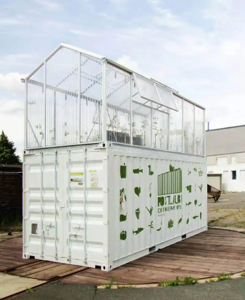 White shipping container base with a glass greenhouse structure on top, used as a sustainable, urban farm or garden.