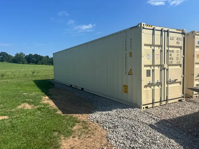A beige shipping container parked on a gravel surface 