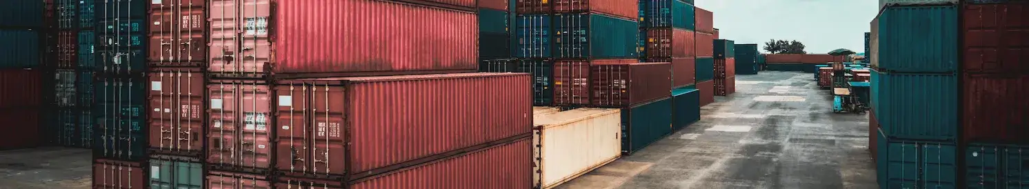 A panoramic view of a massive container yard with tall stacks of red, blue, and brown used shipping containers