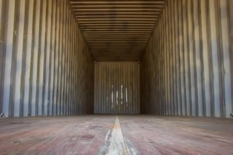 Long view inside an empty used shipping container showing the worn wooden floor planks and ribbed metal walls.
