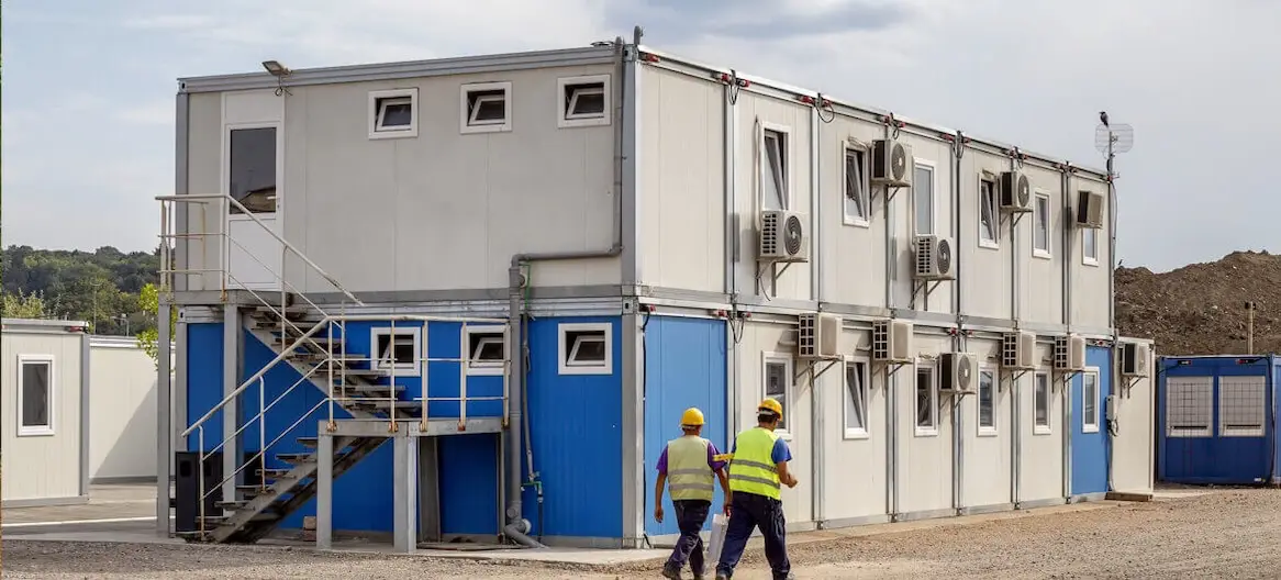 Large two-story modular office building for a construction site with external stairs, many windows, and AC units.