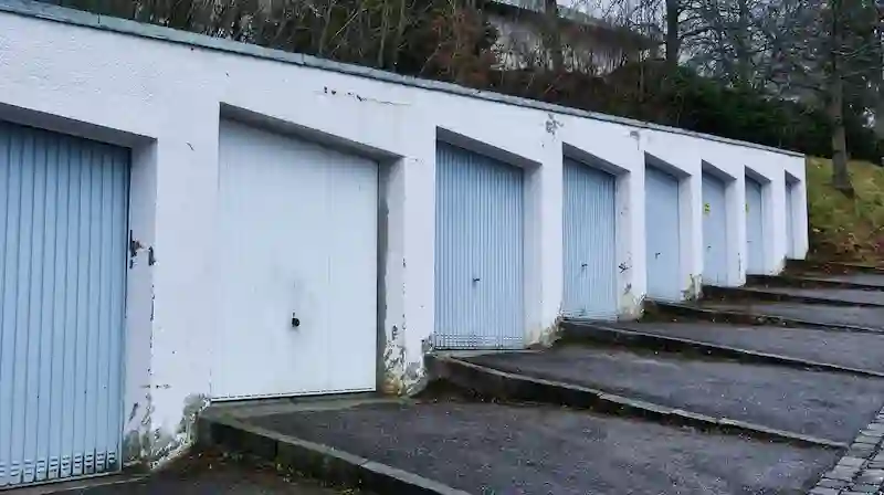 Row of old, run-down garage doors with peeling paint and cracked concrete, representing outdated vehicle storage.
