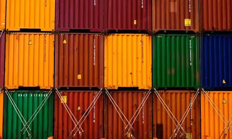 Close-up of tightly stacked multi-colored shipping containers secured with locking rods, symbolizing controlled global inventory.